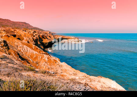 Coucher du soleil sur l'océan turquoise avec Rocky Bay, ci-dessous, et rose-orange ciel au-dessus. Banque D'Images