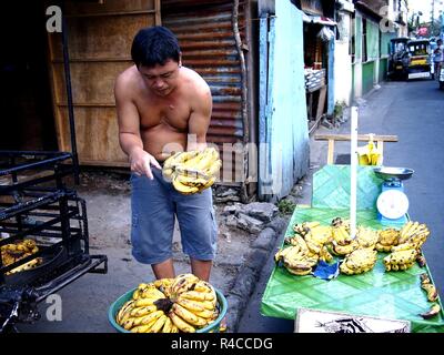 ANTIPOLO CITY, PHILIPPINES - 24 NOVEMBRE 2018 : Un vendeur de fruits prépare les bananes qu'il vend sur son panier de fruits et colporte les accompagner sur une rue animée. Banque D'Images