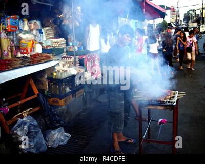 ANTIPOLO CITY, PHILIPPINES - 24 NOVEMBRE 2018 : Un vendeur de nourriture des barbecues barbecue de porc et les vend à son étal de fortune sur un trottoir le long d'une rue animée Banque D'Images