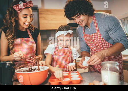 Heureux parents et leur fille sont en train de préparer des cookies ensemble dans la cuisine. Petite fille aide à ses parents de mettre en papier dans des moules. Banque D'Images