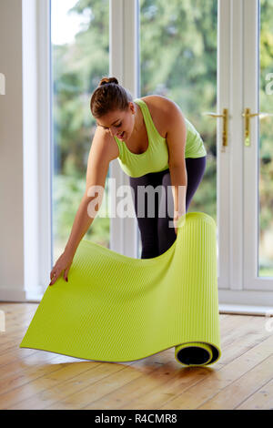 Femme déployant un tapis de yoga Banque D'Images