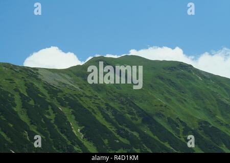 Une vue panoramique d'un Grassy Mountain Ridge contre le ciel avec les nuages qui de derrière la crête de la montagne. Banque D'Images