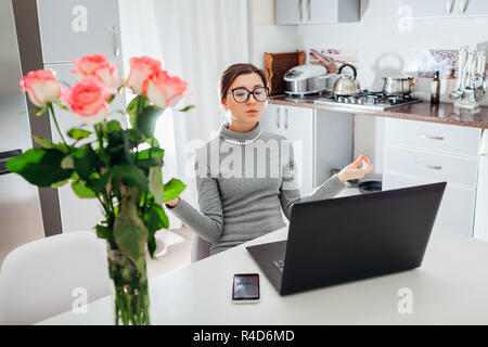 Woman relaxing après avoir travaillé sur ordinateur portable sur cuisine moderne. Les jeunes fatigué freelancer méditer pour se calmer Banque D'Images
