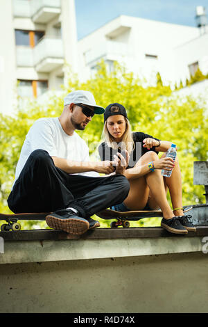 Garçon et fille sur une planche à roulettes sont assis et regarder quelque chose sur le téléphone mobile un jour d'été Banque D'Images