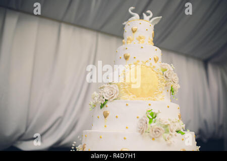 Un grand gâteau de mariage blanc décoré de fleurs d'or et de cygnes blancs. Deux pièces sont coupées. Banque D'Images