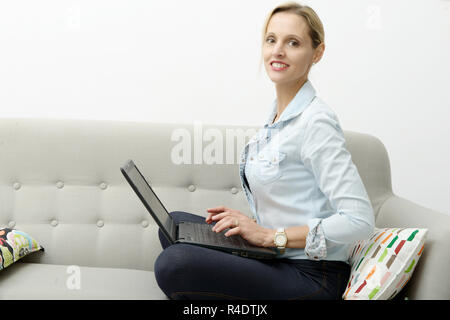 Très belle jeune femme blonde utilise un ordinateur portable dans le canapé Banque D'Images