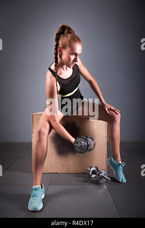 Jeune femme confiante biceps faisant de l'exercice avec haltères en centre de remise en forme. Formation fille mince dans la salle de sport Banque D'Images