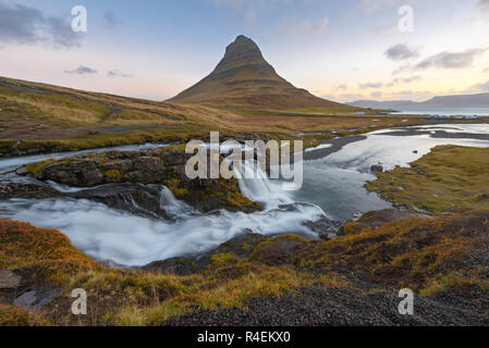 Haut de la sunrise incroyable chute d'Kirkjufellsfoss avec Kirkjufell mountain en arrière-plan sur la côte nord de l'Islande, péninsule de Snæfellsnes pris un long blanc vitesse d'obturation. Banque D'Images