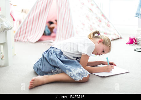Fille assise sur le sol dans sa chambre faire ses devoirs Banque D'Images