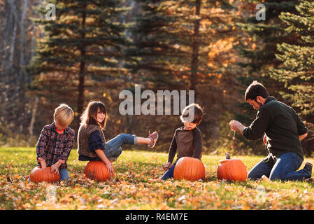 Père et trois enfants carving citrouilles d'Halloween dans le jardin, United States Banque D'Images