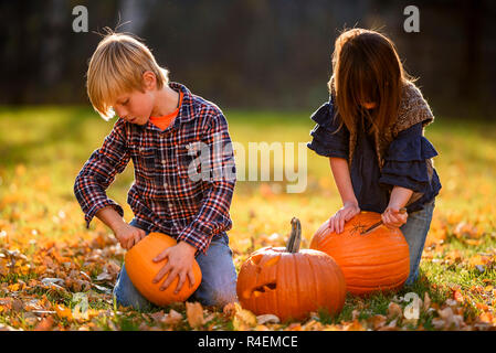 Frère et soeur assis dans le jardin sculpture Halloween pumpkins, United States Banque D'Images