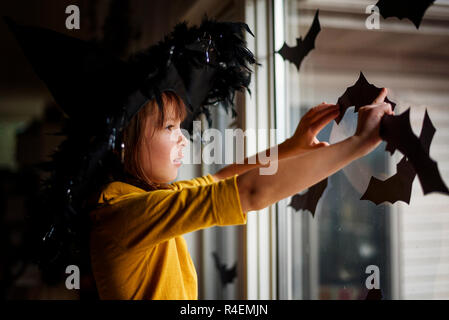 Jeune fille portant un chapeau de sorcière bat coller des décorations sur une fenêtre, United States Banque D'Images