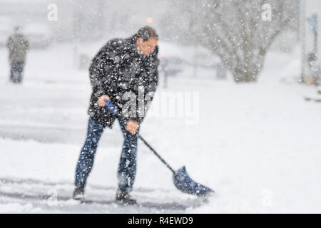 Jeune homme de flou artistique, homme en manteau d'hiver, le nettoyage, l'entrée de pelleter la neige dans la rue à partir de la tempête de neige lourde, tenant une pelle, maisons d'habitation Banque D'Images