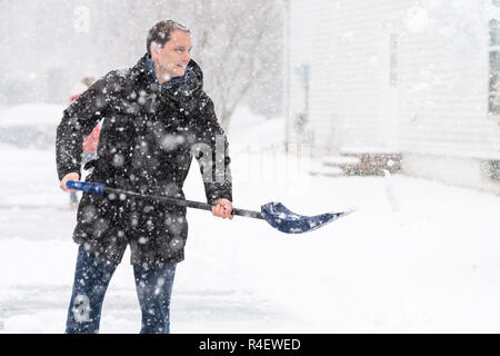 Heureux, jeune homme, homme en manteau d'hiver, de lancer le nettoyage, pelleter l'entrée, de la rue couverte de neige, chute de neige lourde tempête de wit Banque D'Images