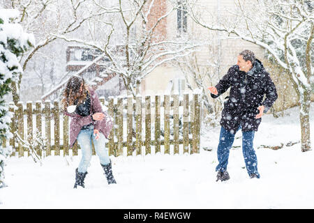 Jeune homme, femme jouant, jetant des boules de volant en l'air, de l'air dans une tempête de neige d'hiver, à la maison, maison jardin, cour avant, arrière-cour, arbres couvrir Banque D'Images