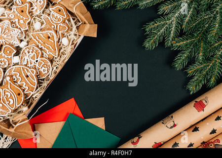 Concept de Noël. L'espace pour le texte. Gingerbread cookies dans le présent fort, lettres, enrouler du papier et branches de sapin sur le fond noir tableau. Haut de la vie Banque D'Images