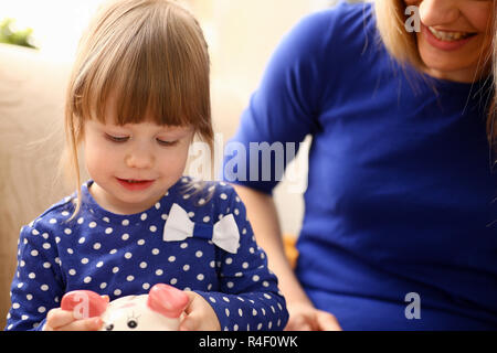 Le bras de l'enfant petite fille mettre des pièces en piggybank Banque D'Images