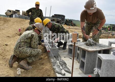 3e classe constructeur Franklin Alexis travaille avec les caporaux Giurca, Szabo, et de la Vagu 10e Brigade Ingénieur roumain comme ils place des blocs de béton pour le mur d'un bâtiment de stockage et d'opérations dans le cadre de Resolute Château 17 au Centre national de formation conjointe, Cincu, Roumanie, tandis que Samantha Kylberg 3e classe Builder fournit le mortier. Château ferme 17 est un exercice le renforcement de l'alliance de l'OTAN et de renforcer sa capacité de formation conjointe et de réponse aux menaces dans la région. Banque D'Images