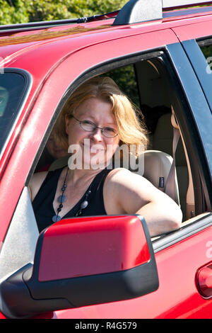 Smiling woman conduit une voiture rouge Banque D'Images