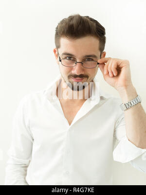 Bel homme intelligent holding glasses stand against white background. L'homme penché, dans les verres et chemise blanche, portrait. Close up Smiling Young Businessman Wearing Eyeglasses. Banque D'Images