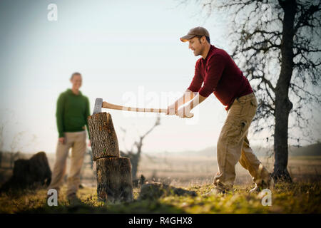 Jeune adulte homme couper du bois avec une hache dans un champ. Banque D'Images