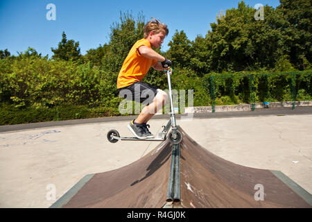 Boy saute avec un scooter sur une colonne vertébrale dans le skate parc et d'en profiter Banque D'Images