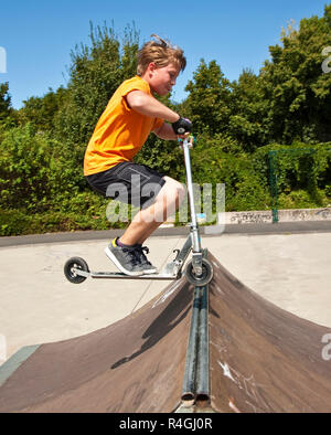 Boy saute avec un scooter sur une colonne vertébrale dans le skate parc et d'en profiter Banque D'Images