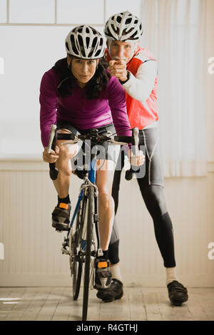 Femme mature pratiquant le vélo à l'intérieur, alors que les plus âgés l'homme demande à son Banque D'Images