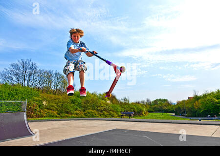 Boy saute avec un scooter sur une colonne vertébrale dans le skate parc Banque D'Images