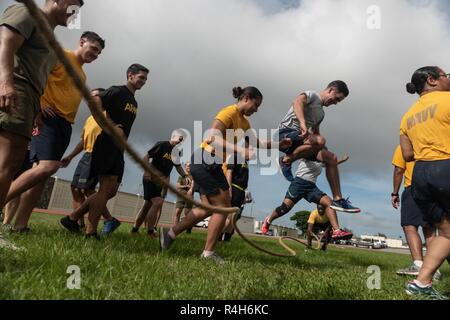 Les soldats, marins, aviateurs et marines de sauter par-dessus une corde pendant le Défi de remise en forme mixte d'Okinawa, le 26 septembre 2018, à Kadena Air Base, au Japon. Corde à sauter le défi exige de tous les 48 élèves à saute sur la corde s'il est en mouvement. Si la corde a touché un étudiant alors qu'ils sautaient dessus, ou si la corde est arrêté, les élèves devraient commencer plus d'encore. Banque D'Images