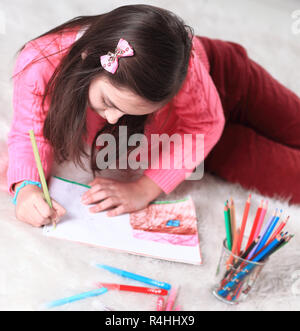 Petite fille peint avec des pinceaux, gisant sur le sol dans la salle de séjour Banque D'Images