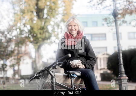 Portrait d'une femme assise sur un banc avec un verre à côté d'un vélo, Allemagne Banque D'Images