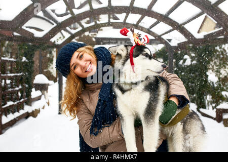 Authentique attractive caucasian woman hugs funny chien malamute wearing santa chers bois de noël. Female bouclés s'amusant avec chiot huskies sur nouvelle année. Le Pet est meilleur cadeau pour les vacances. Banque D'Images