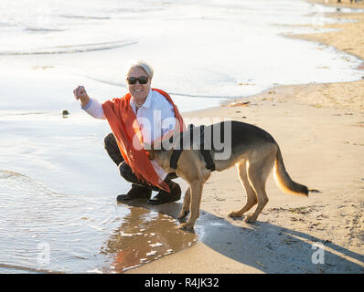 Belle veuve vieille femme jouant avec son chien shepard allemand bénéficiant de son compagnon et de l'amour sur la plage au coucher du soleil dans les avantages de garder les animaux à acti Banque D'Images
