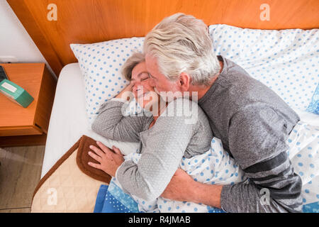 Couple âgé à la retraite de 70 ans dans le lit à s'embrasser et se réveiller tôt le matin avec l'amour et la tendresse - les gens vivre pour toujours ensemble d'hiver Banque D'Images