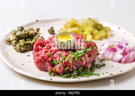 Tartare de boeuf à l'oeuf de caille, la coupe shell concombres, câpres, oignon rouge, ciboulette, salade de roquette et servi dans des assiettes en céramique avec pep tacheté Banque D'Images