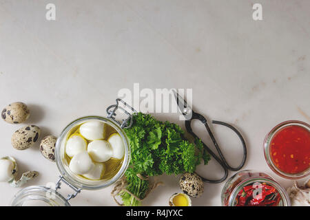 Ingrédients pour des oeufs de caille marinés au vinaigre. Oeufs durs à l'huile d'olive, sauce tomate, piments en pots, persil frais, des ciseaux sur whi Banque D'Images