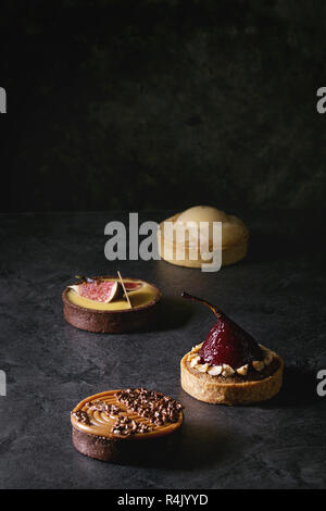 Variété de sweet tartelettes au chocolat, caramel, poires, figues sur noir table de texture. Banque D'Images