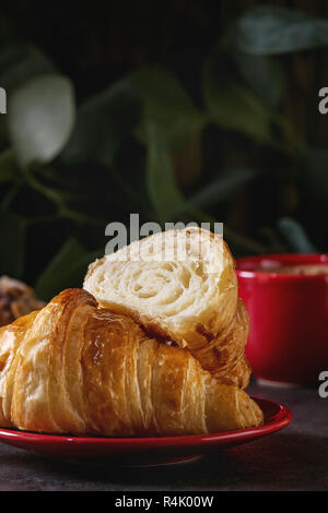 Tout frais cuit et tranché un croissant rouge avec tasse de café espresso sur tableau noir à l'eucalyptus. Style rustique foncé. Close up Banque D'Images