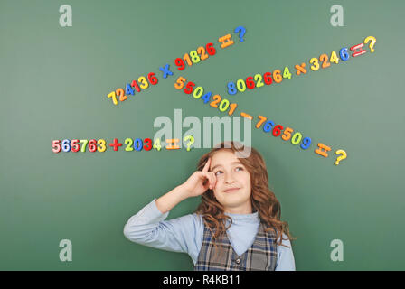 Jeune fille se tient devant un conseil de l'école verte avec des aimants de chiffres qui illustrent ses pensées sur fond vert Banque D'Images