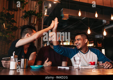 Heureux l'arabe young man giving high five à son ami. Les personnes de race mixte de groupe s'amusant dans le salon bar. Les amis se détendre et de rire Banque D'Images
