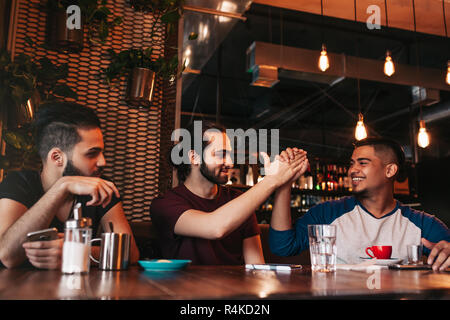 Heureux jeune homme arabe haute donnant cinq à son ami. Les personnes de race mixte de groupe s'amusant dans le salon bar. Lieu d'amis et de rire Banque D'Images