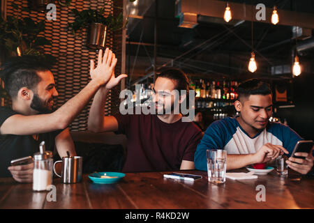 Heureux jeune homme arabe haute donnant cinq à son ami. Les personnes de race mixte de groupe s'amusant dans le salon bar. Lieu d'amis et de rire Banque D'Images