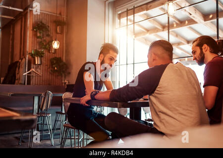 Groupe de jeunes hommes de race mixte à parler dans un bar-salon. Avoir de bons amis multiraciale temps à communiquer dans un café et de boire du café Banque D'Images