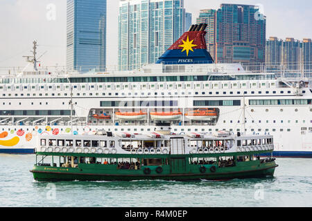 Un vert et blanc traditionnel Star Ferry en face d'un grand bateau de croisière dans le port de Victoria, Hong Kong Banque D'Images