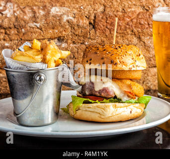 Fruits de mer et viandes burger avec anneaux de calmars frits, fromage fondu, bacon croustillant et d'un boeuf patty servi sur un plateau avec des croustilles de pommes de terre dans un seau. Banque D'Images