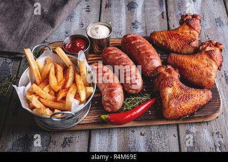 Ailes de poulet grillées, saucisses, frites, sauce rouge et blanc sur une surface en bois Banque D'Images