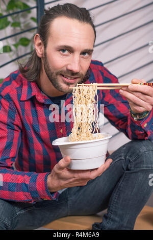 L'homme en chemise à carreaux assis dans les escaliers et de manger la nourriture asiatique Banque D'Images