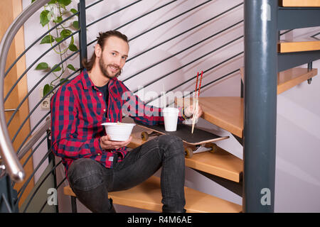 L'homme en chemise à carreaux assis dans les escaliers et de manger la nourriture asiatique Banque D'Images