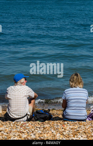 D'âge moyen ou vieux couple assis au soleil sur une plage de galets ou de cailloux dans la canicule de l'été sur l'île de Wight. Banque D'Images